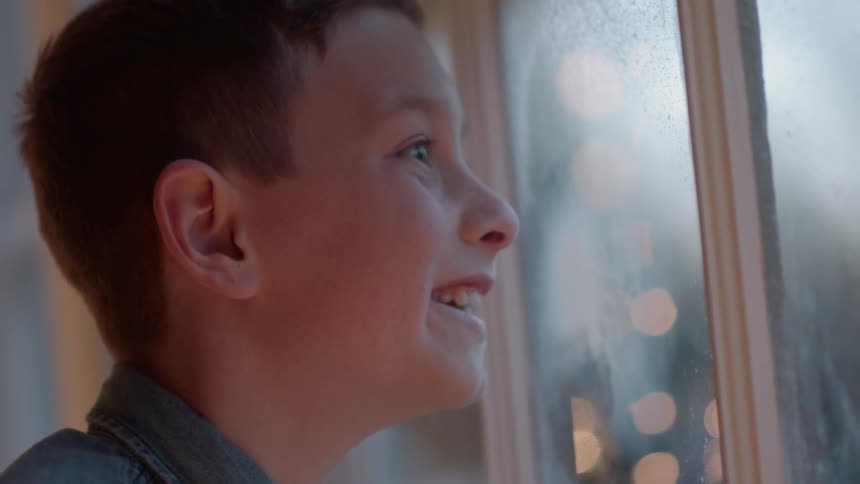 A boy smiles and looks out a window on christmas