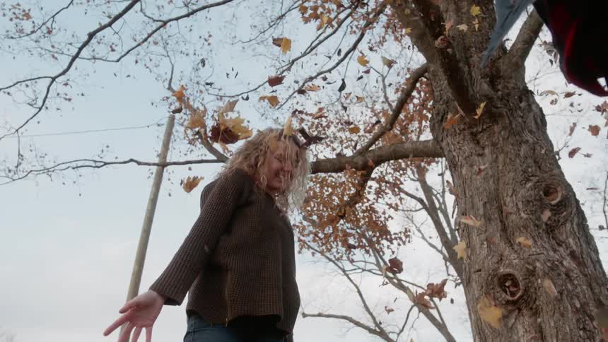 A woman extends her arms as a friend tosses leaves into the air