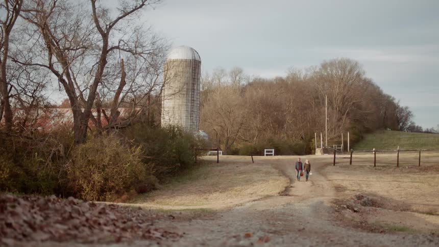 Man and woman walk towards a silo carrying pumpkins