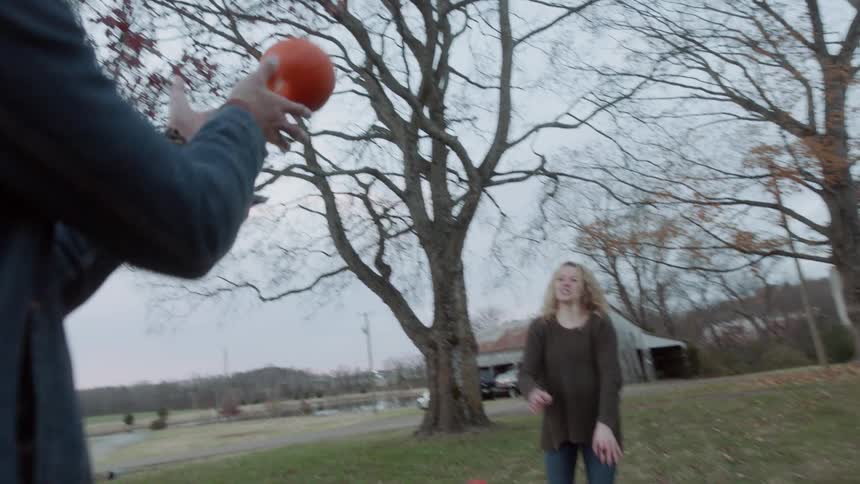 Man and woman toss a small pumpkin to one another