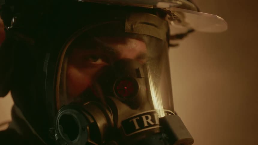 A firefighter wears a helmet and mask in a smoky room