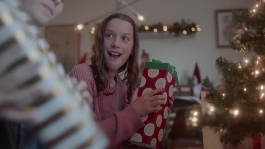 A brother and sister look at and shake gifts from under the tree