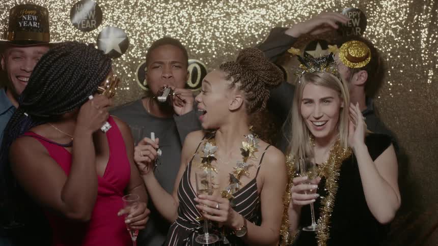 A group of friends laugh and blow noisemakers on new year's eve