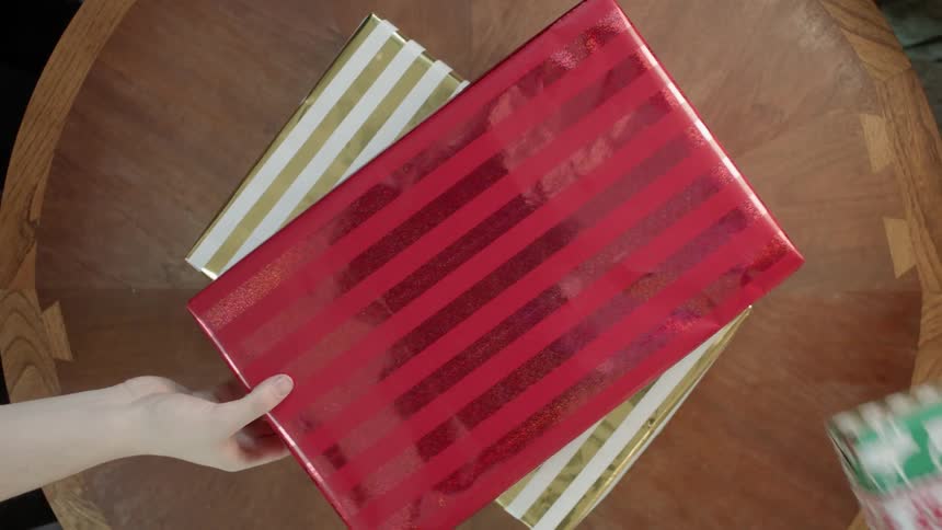 Hands reach out and remove wrapped christmas presents from a table