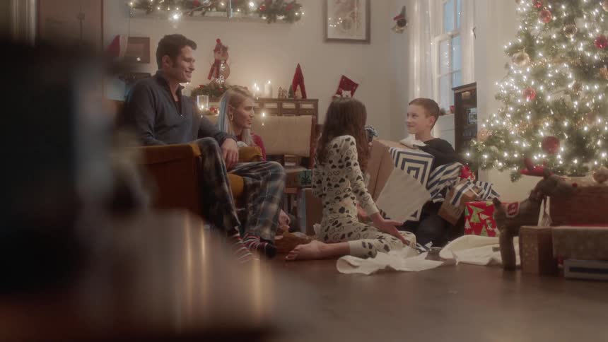 A family is sitting around a Christmas tree and opening presents