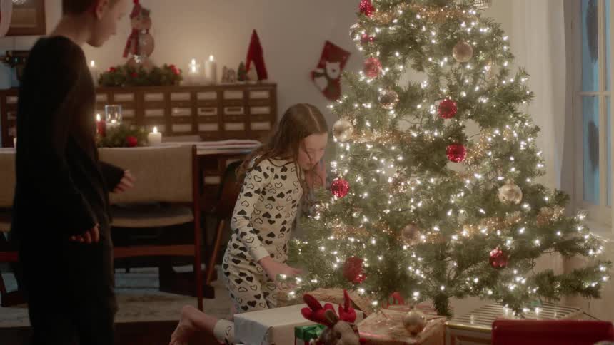 A girl and boy kneel next to a christmas tree