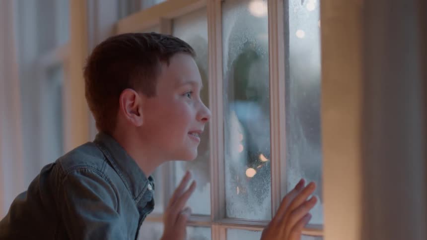 A boy looks out a window on a snowy day