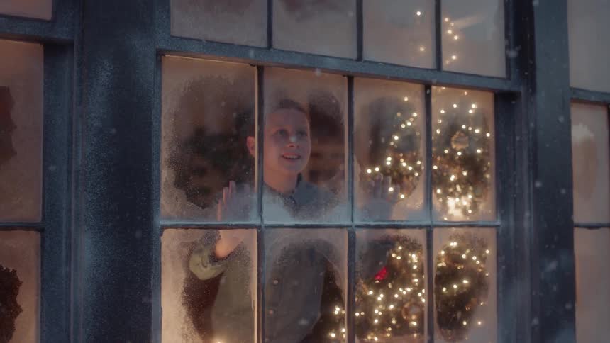 A boy looks out the window at the falling snow at christmas time