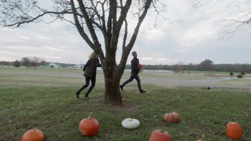 A man and woman run playfully around pumpkins