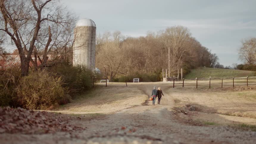Man and woman walk towards a silo carrying pumpkins