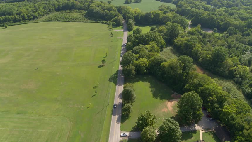 Cars travel on a road next to a grass field and trees