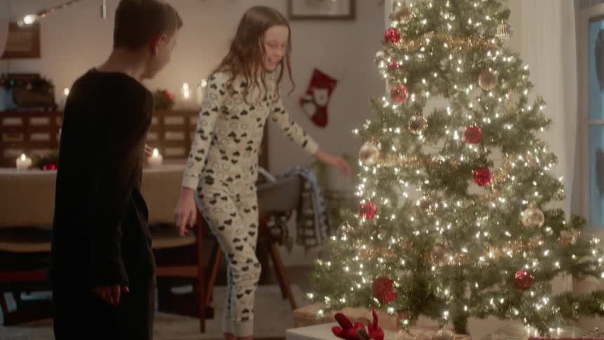 A boy and girl run to look at presents next to a christmas tree