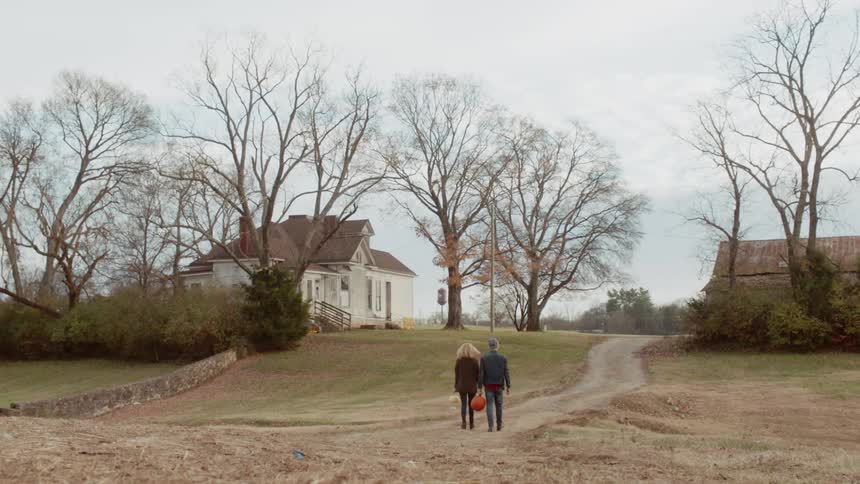 A man and woman walk towards a house while carrying pumpkins