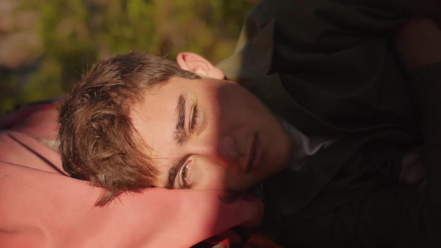 Man wakes up as the sun hits his face he shields it with his hand