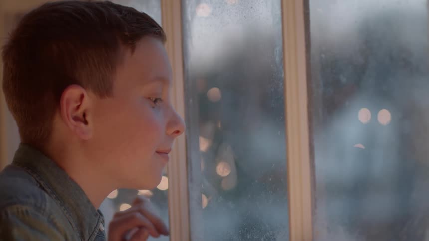 A boy looks out a window at the falling snow