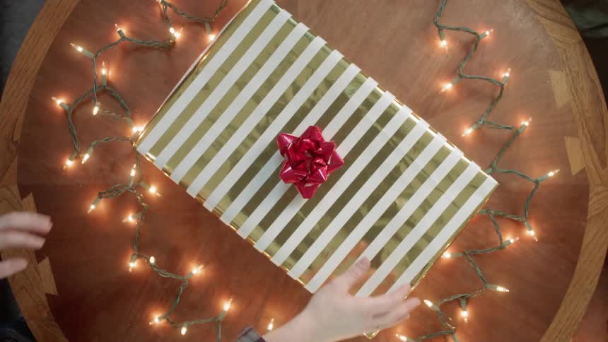 A person puts a wrapped gift down on a table another sticks a bow on it