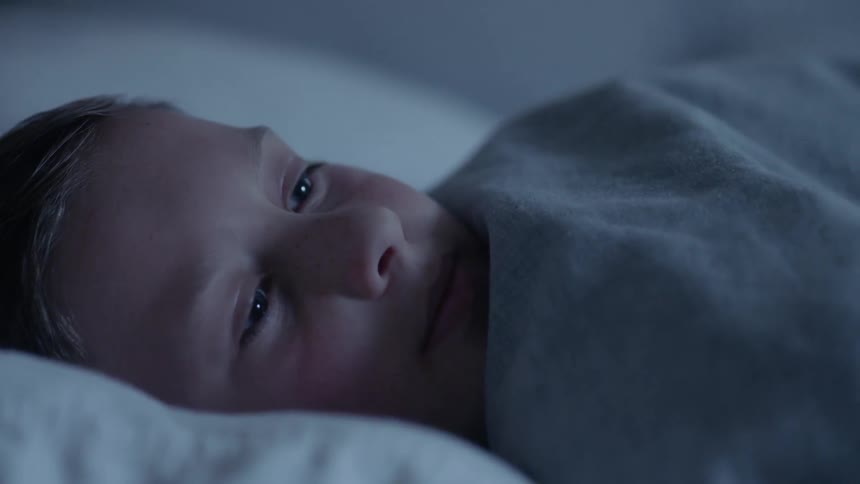 A sleeping boy wakes up and smiles then gets up