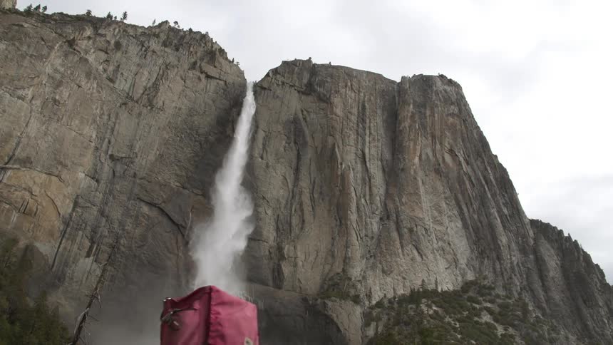 A hiker walks towards a waterfall gushing from a cliff