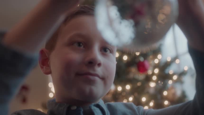 Boy in front of christmas tree shakes snow globe