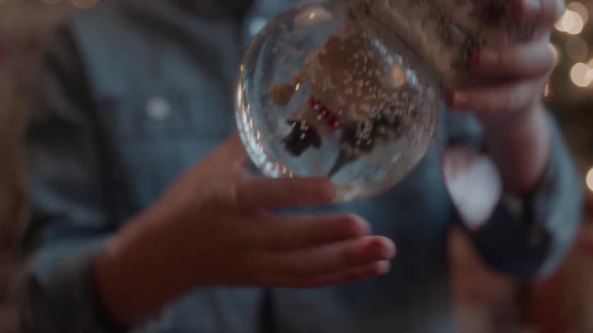 A young boy turns a snow globe upside down next to a christmas tree
