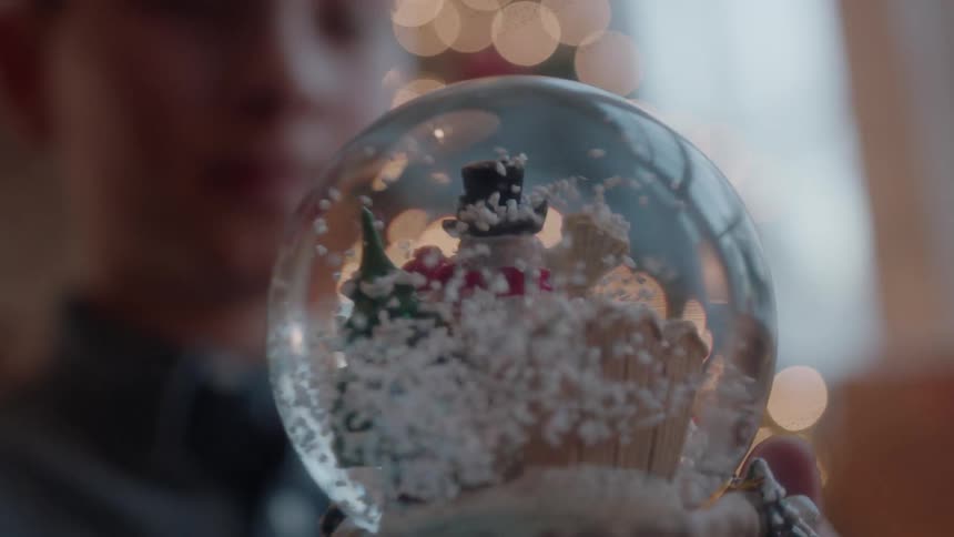 A boy holds a snow globe next to a christmas tree