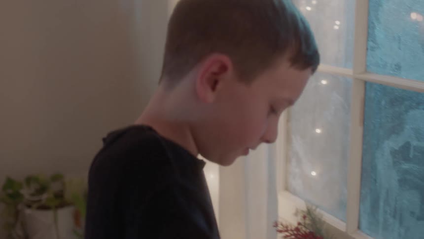 A boy grabs a christmas stocking and puts candy canes on a windowsill