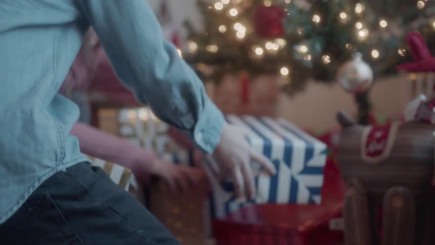 A boy and girl put presents under a christmas tree