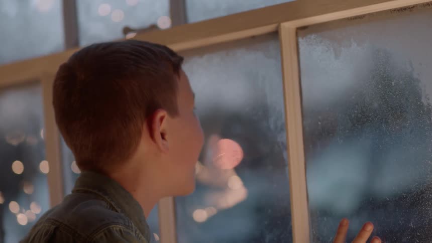 Boy looks out window at snow on christmas