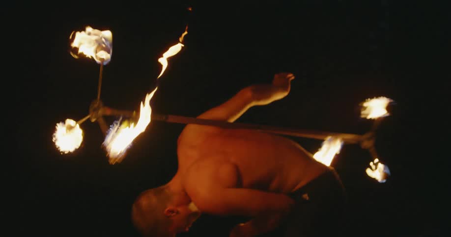 A man twirls torches on a pole at night