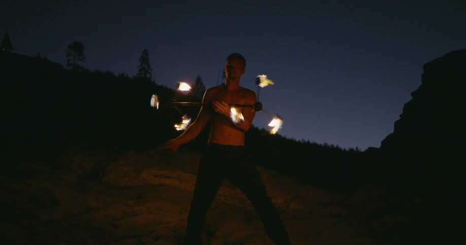 Man spins a burning pole with spinners on each end