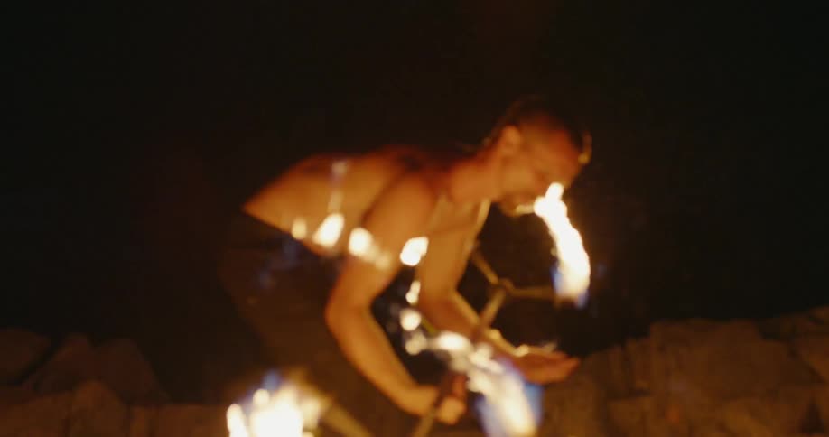 A man twirls a rod with fire on each end
