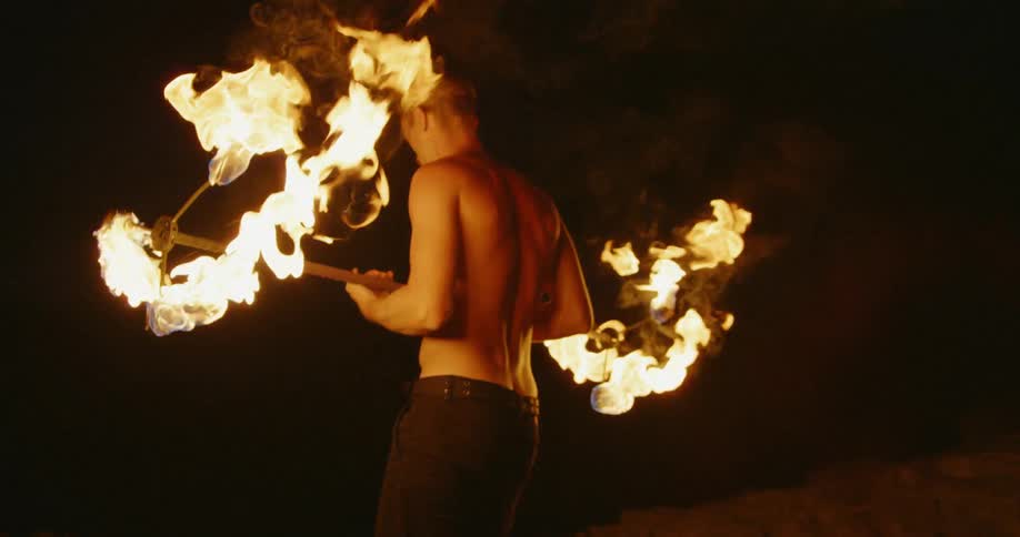 Man holds a poi pole with burning spinners on each end