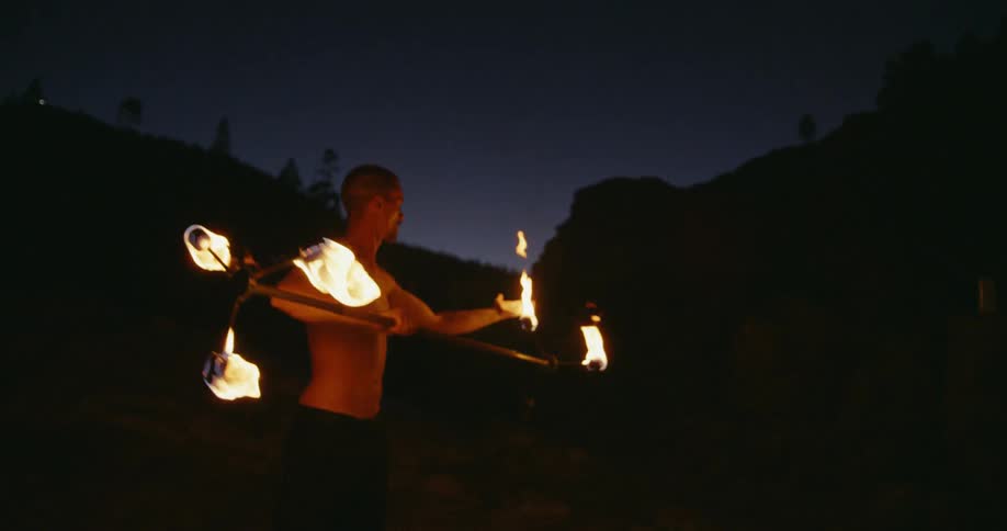 A shirtless man lights his staff on fire with his hand