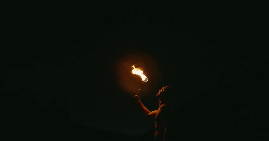 A man holds a flaming torch up at night