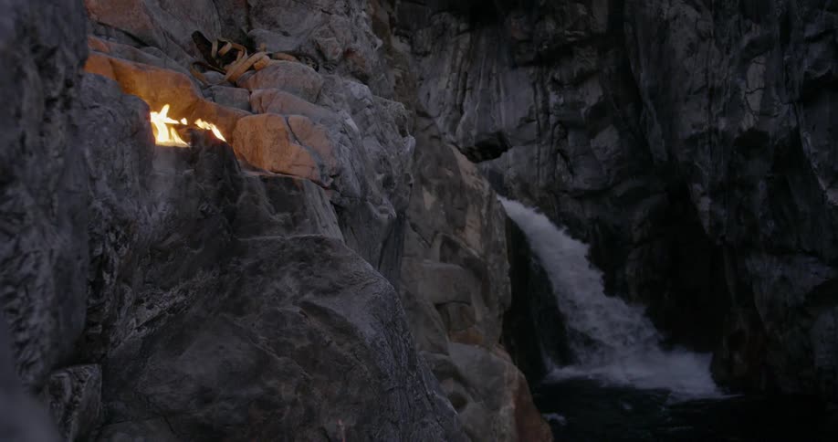 Fire burns in granite rocks next to waterfall at night