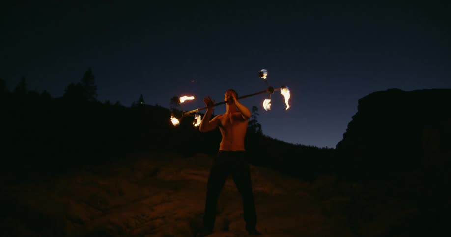 Man using a lighted baton-like device to perform on a dark area outdoors