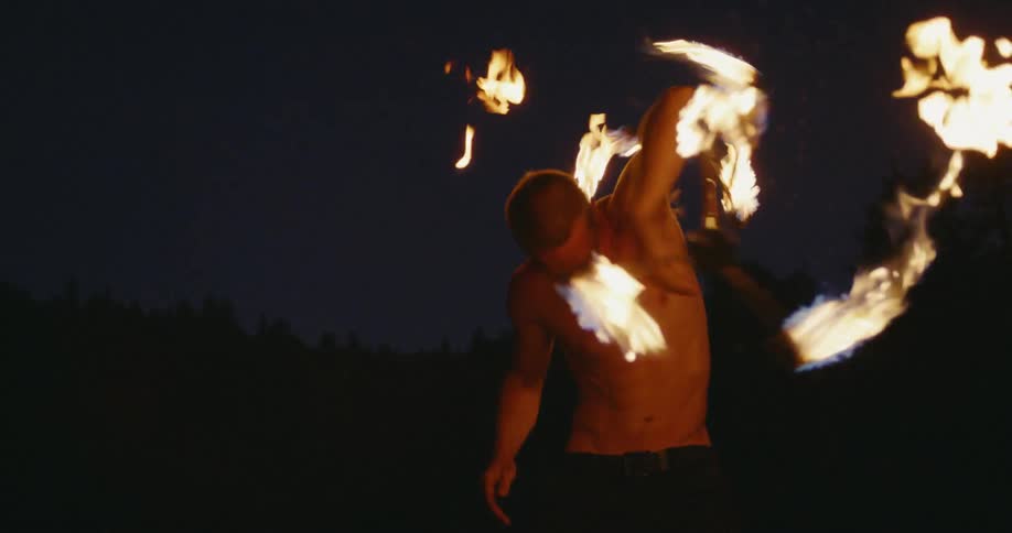 A man is twirling and balancing flaming torches at night
