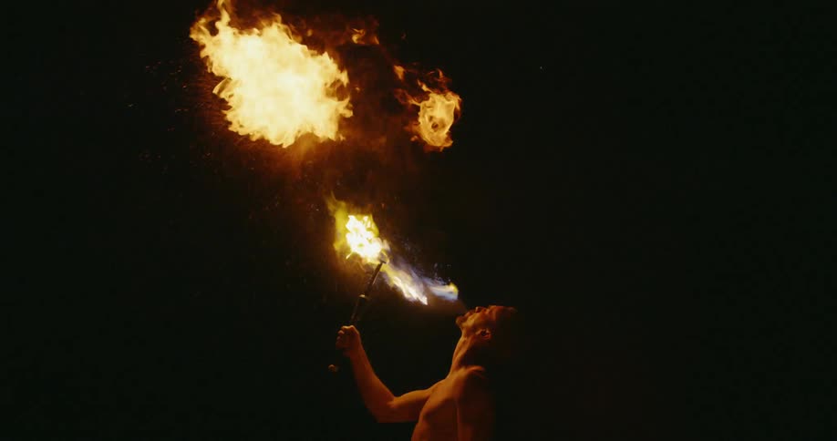A man is blowing fuel into a burning torch to make a fireball