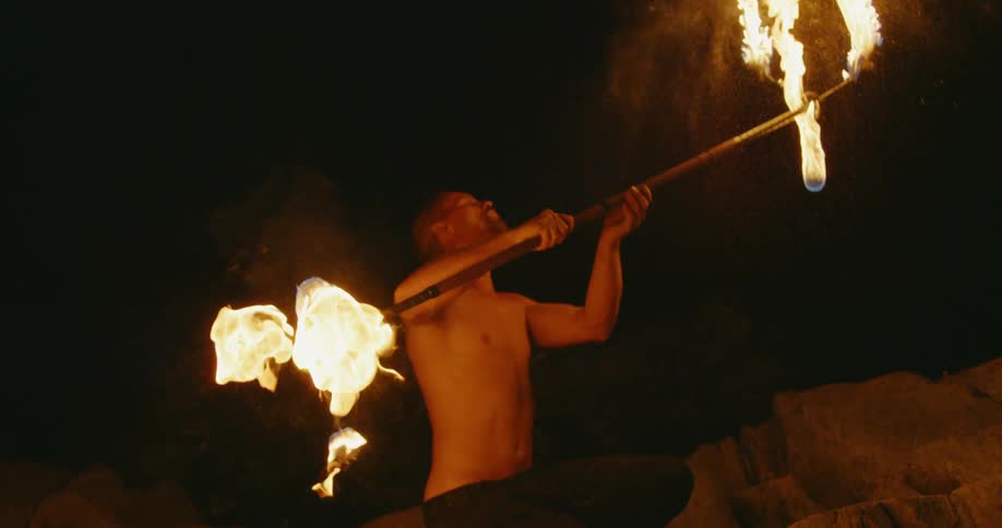 A man is twirling and balancing a bar with flaming torches at night