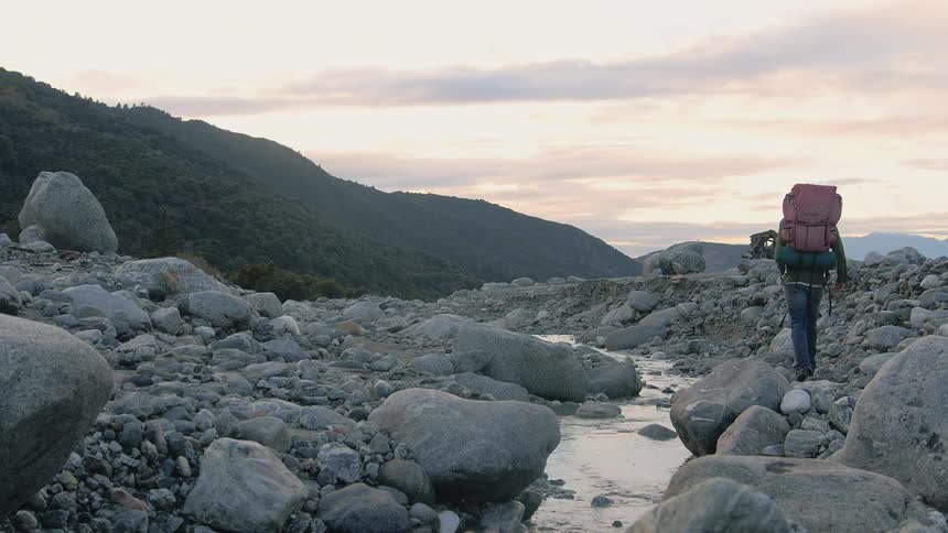 A backpacker hikes alongside a creek in a field filled with rocks and boulders