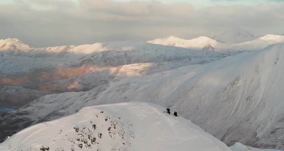 Skiers hike up a snowy mountain at sunset