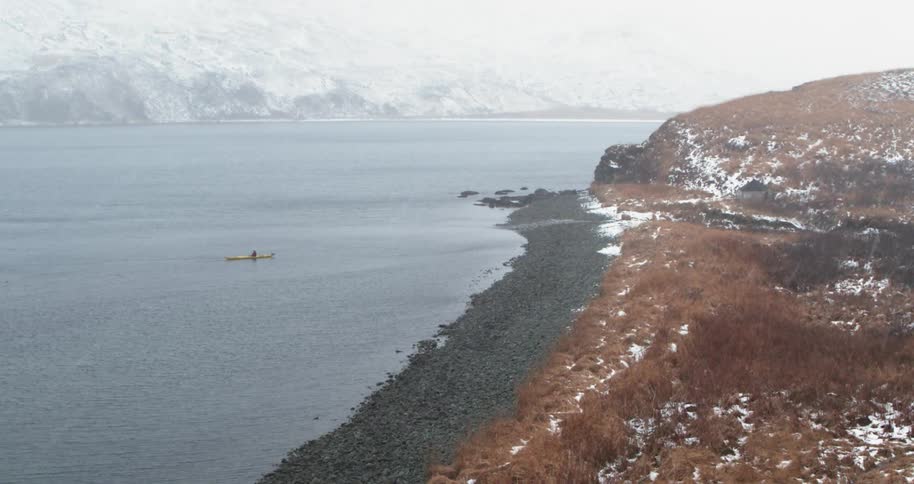 A person kayaks on the sea while it snows
