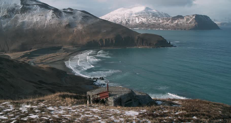 Waves wash ashore near snowy mountains and a bunker