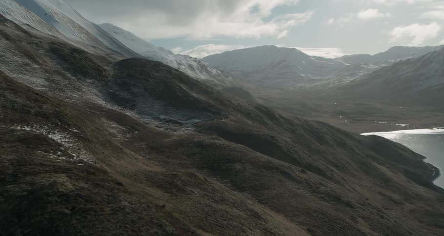 Clouds are hanging over a mountain range and coastline during the day
