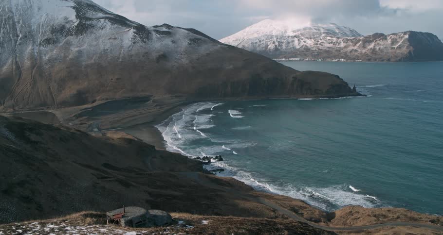 Waves are crashing ashore and large mountains are in the distance
