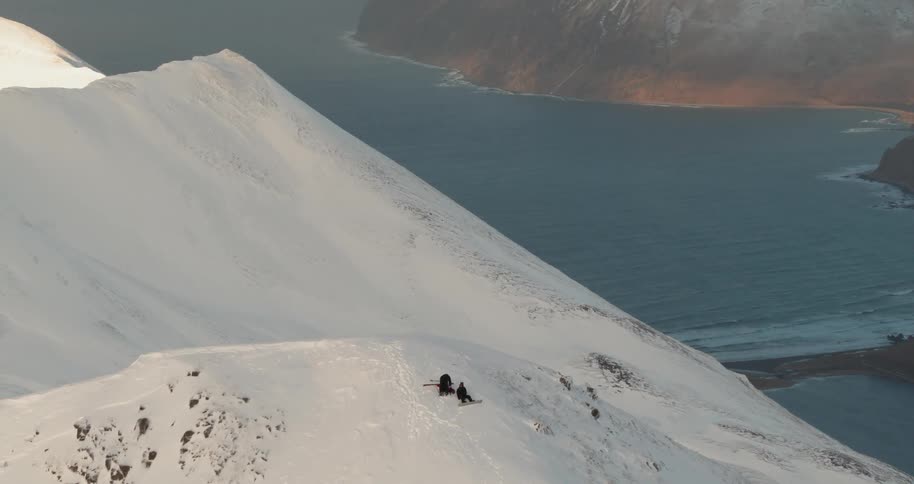 Two skiers rest atop a mountain above the sea