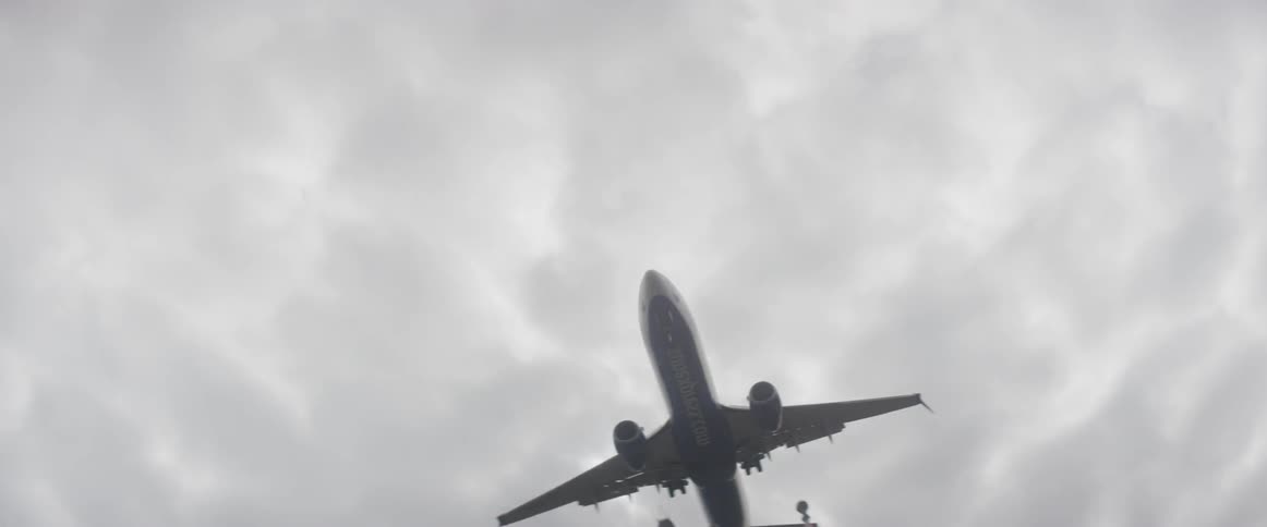 An airplane flies low over a fence and signal lights