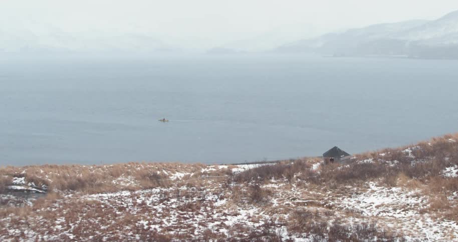 A person sits in a kayak offshore as the snow falls