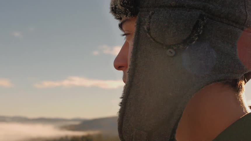 A young man puts on a hat as he stares off into the distance on a sunny day