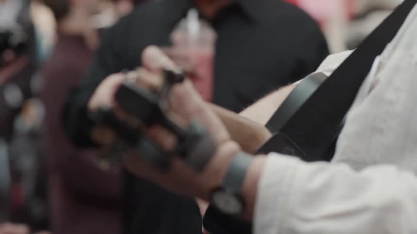 A man plays guitar and another man drinks a pink drink with a crowd of people around them